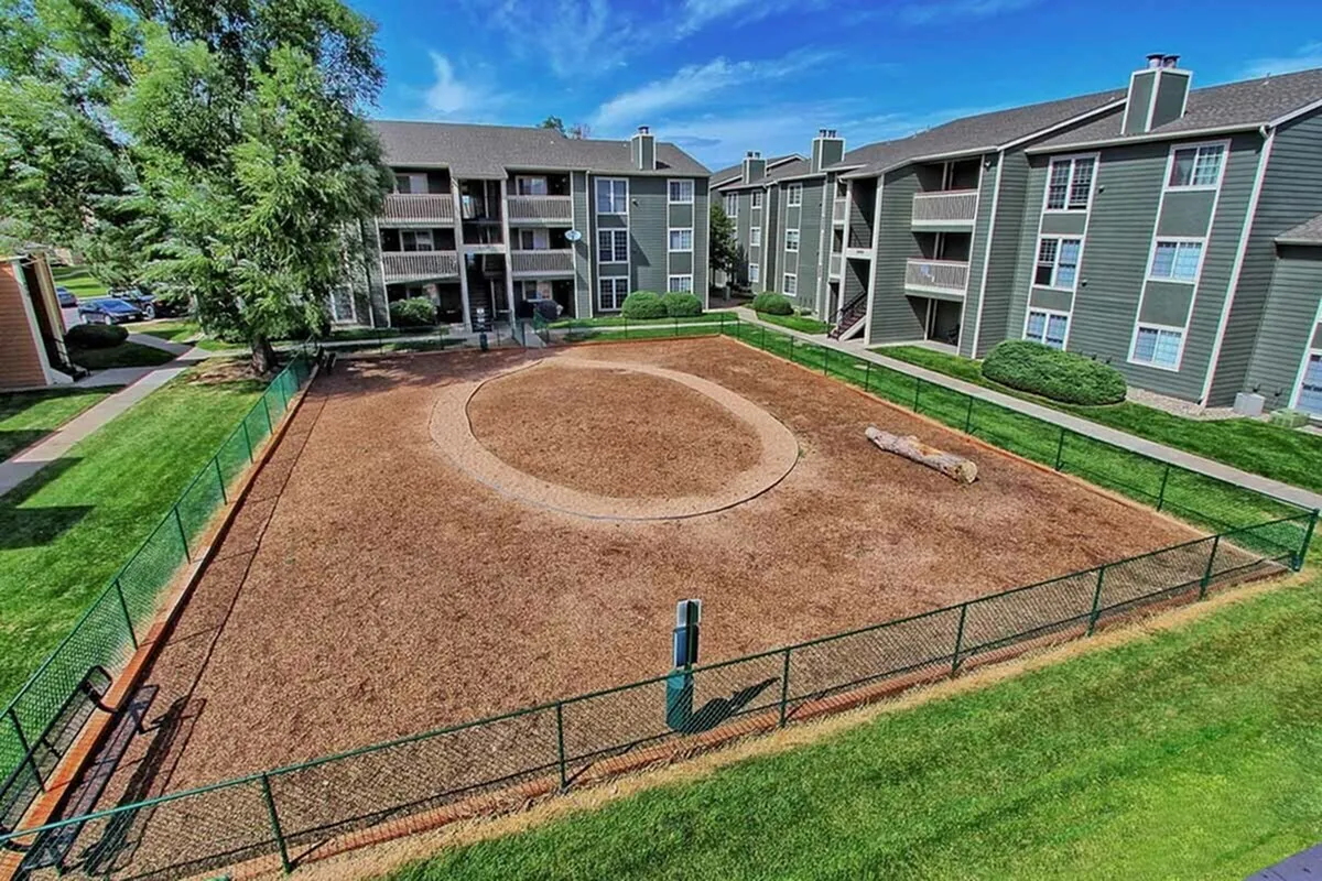 Charming apartment complex with modern balconies overlooking a spacious fenced play area surrounded by lush greenery and vibrant landscaping.