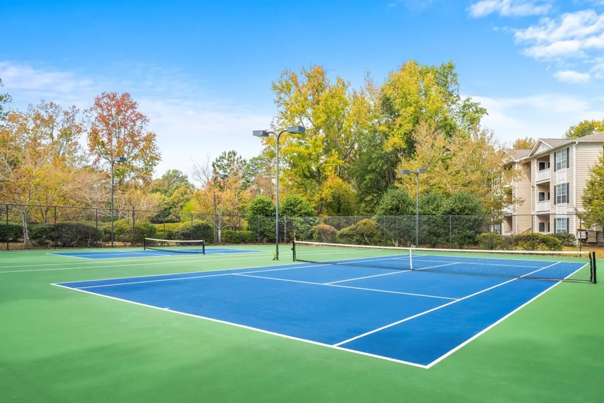 Vibrant outdoor tennis court surrounded by lush greenery, perfect for active living in a scenic apartment community.