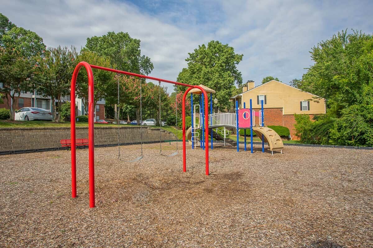 Charming playground with vibrant red swings and a fun adventure play set, nestled in a lush, green community setting.
