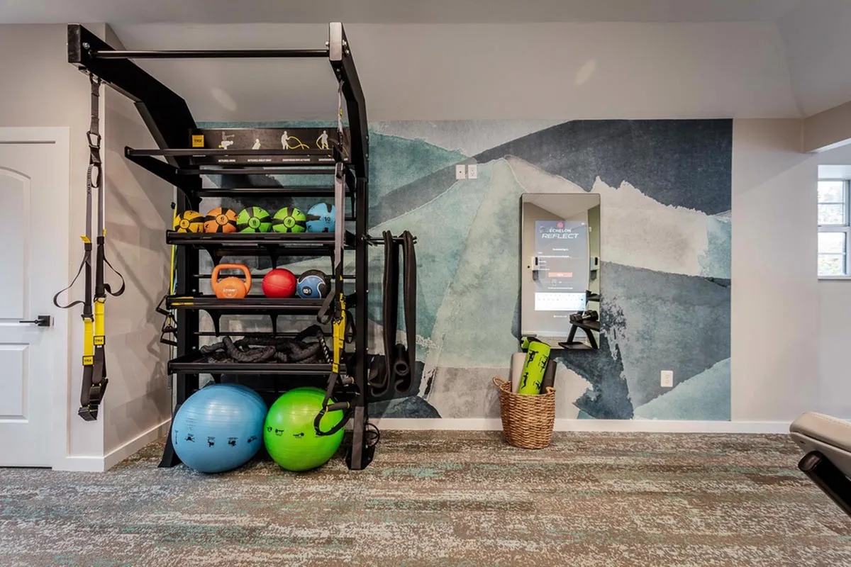 Modern fitness room with a sleek rack of colorful exercise equipment, including TRX bands, kettlebells, and stability balls, against a stylish abstract mural.