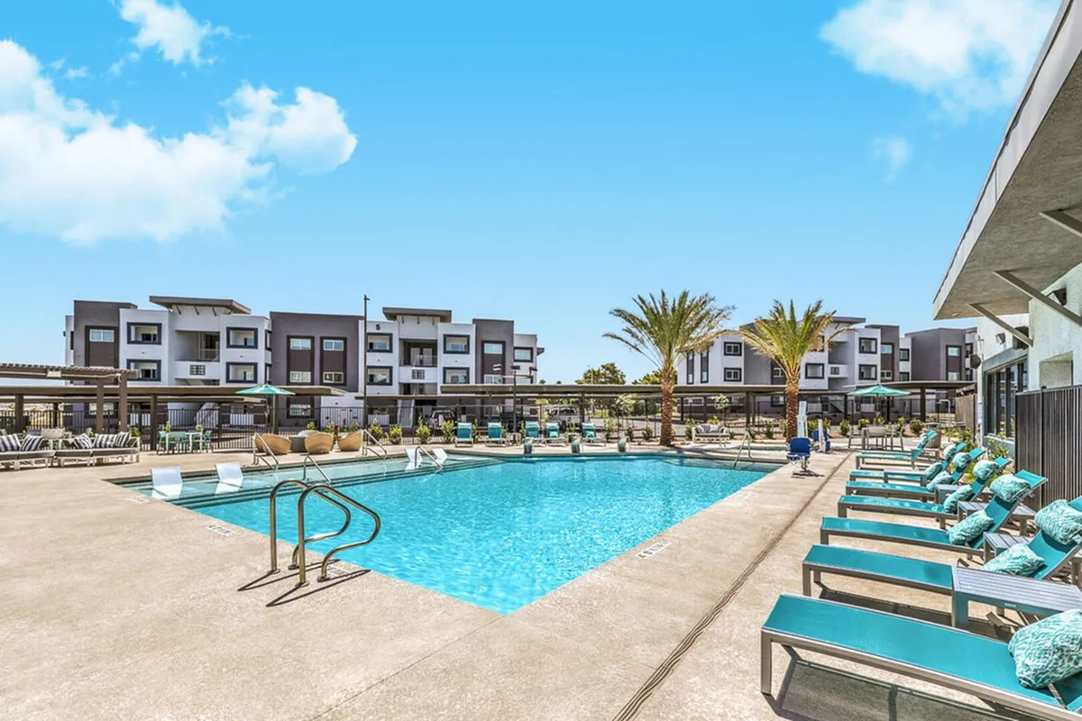 Luxurious apartment complex featuring a sparkling swimming pool, palm trees, and modern architecture under a clear blue sky.