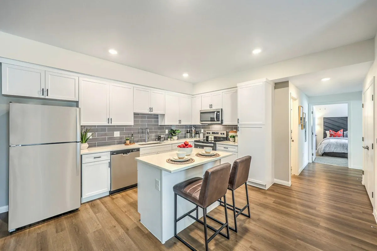 Modern kitchen with elegant white cabinetry, stainless steel appliances, and a cozy island breakfast bar, leading to a charming bedroom with plush bedding.