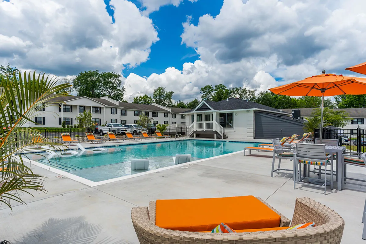 Luxurious outdoor pool area with vibrant orange loungers and umbrellas, perfect for relaxation and leisure, surrounded by lush greenery and modern apartments.