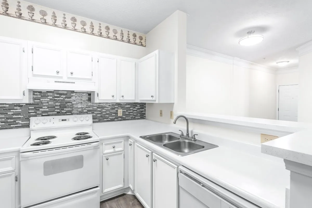 Modern kitchen with white cabinetry, stainless steel sink, and chic mosaic backsplash, offering sleek design and functionality.