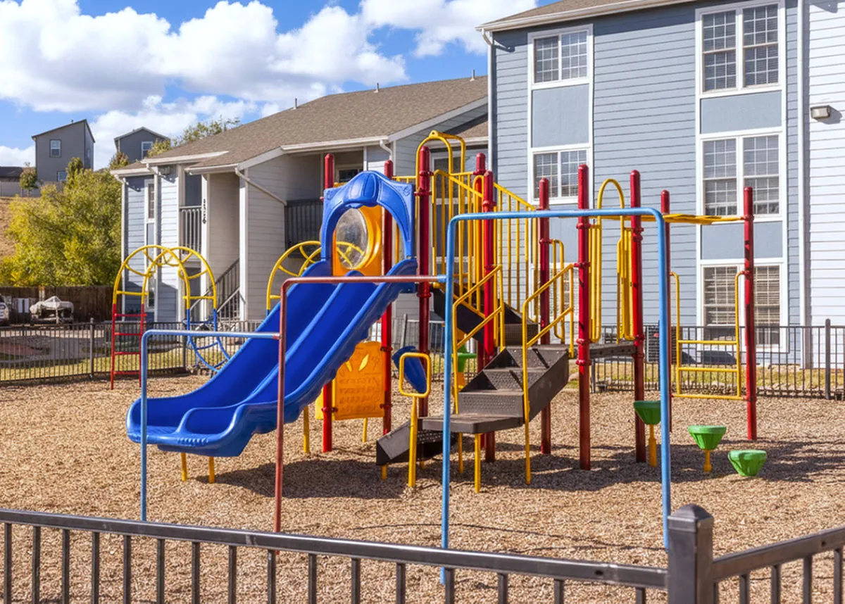 Vibrant playground with colorful slides and climbing structures, nestled beside charming residential buildings under a clear blue sky.