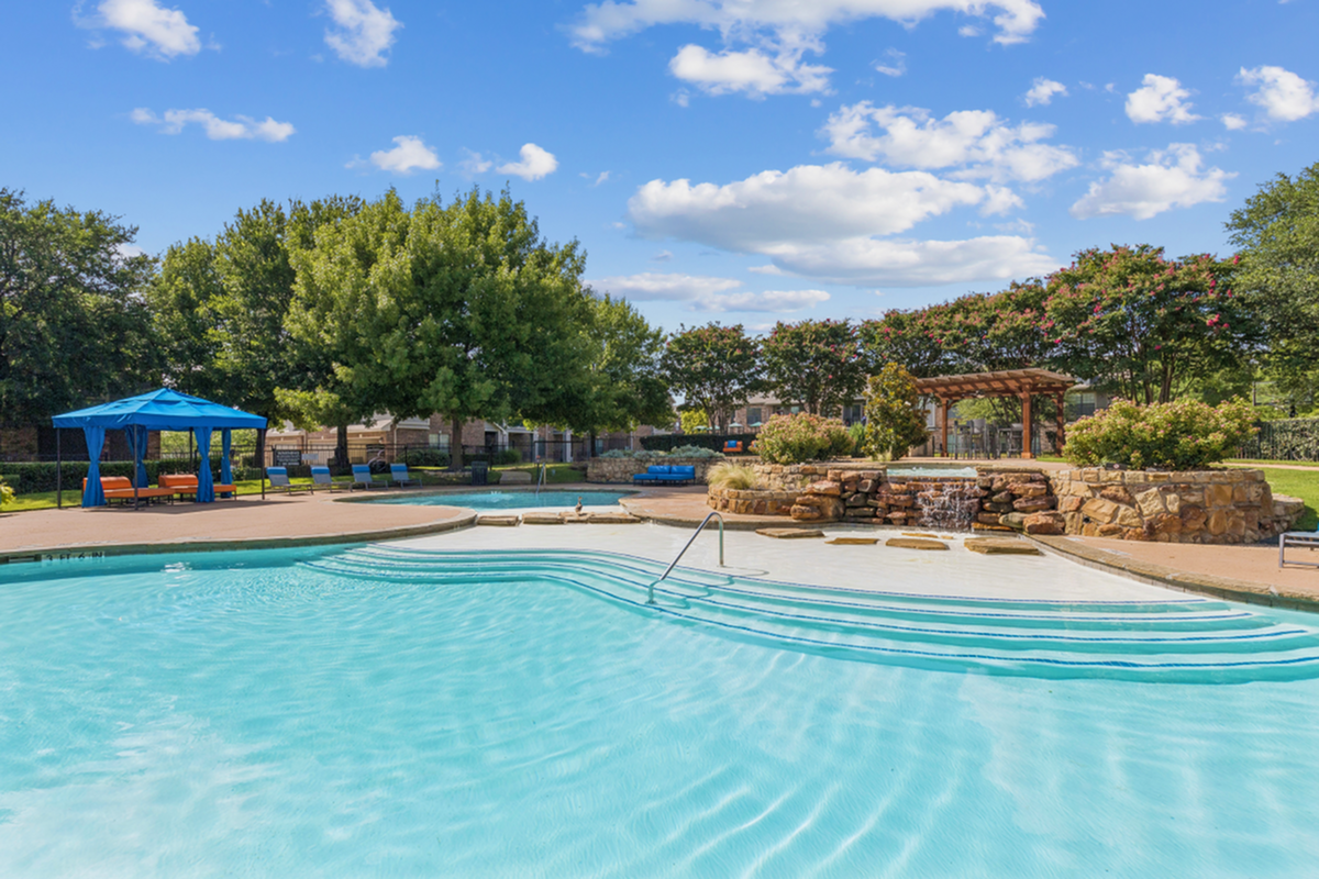 Inviting outdoor pool area with crystal-clear water, a charming waterfall feature, and cozy cabana seating under a vibrant blue canopy.