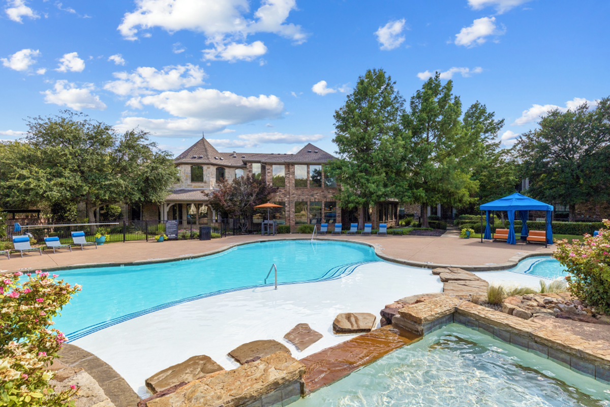 Luxurious apartment complex featuring a large, sparkling pool with a cozy gazebo and lush greenery, perfect for relaxation and recreation.