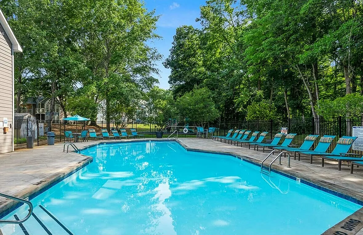 Inviting outdoor pool area surrounded by lush greenery, featuring stylish turquoise lounge chairs, perfect for relaxation and leisure.