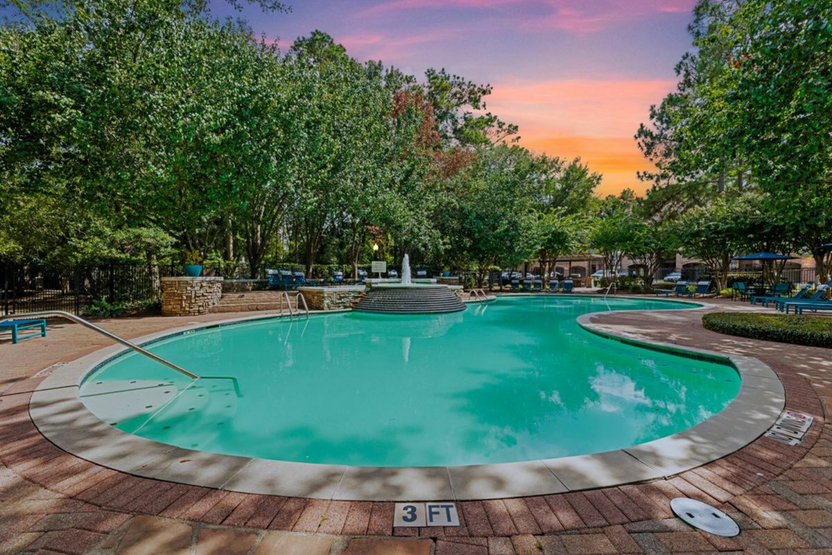 Inviting outdoor pool area surrounded by lush greenery and vibrant seating, perfect for relaxation under a stunning sunset sky.