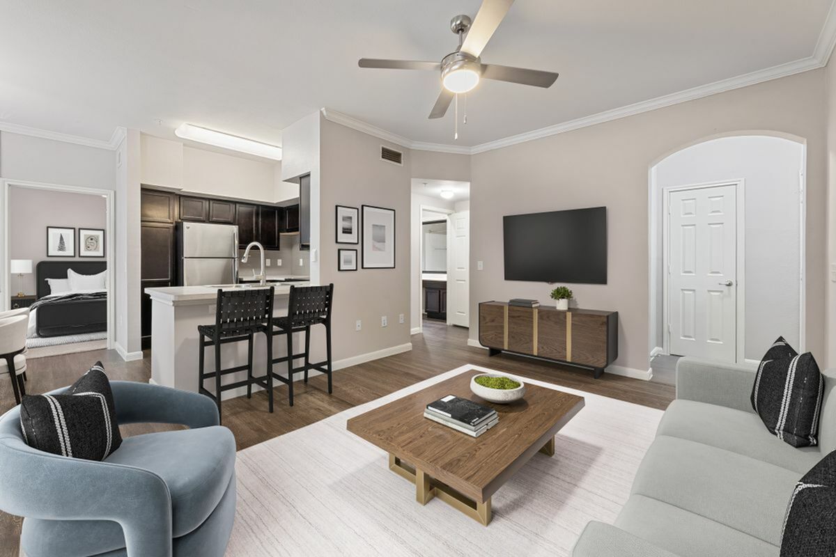 Modern open-concept living room with stylish furnishings, breakfast bar, and sleek kitchen featuring dark cabinetry and stainless steel appliances.