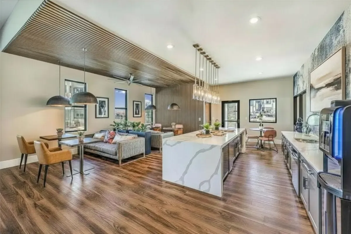 Modern open-concept living space featuring a luxurious kitchen with marble countertops, elegant pendant lighting, and a stylish dining area with cozy seating, set against a backdrop of rich wood flooring.
