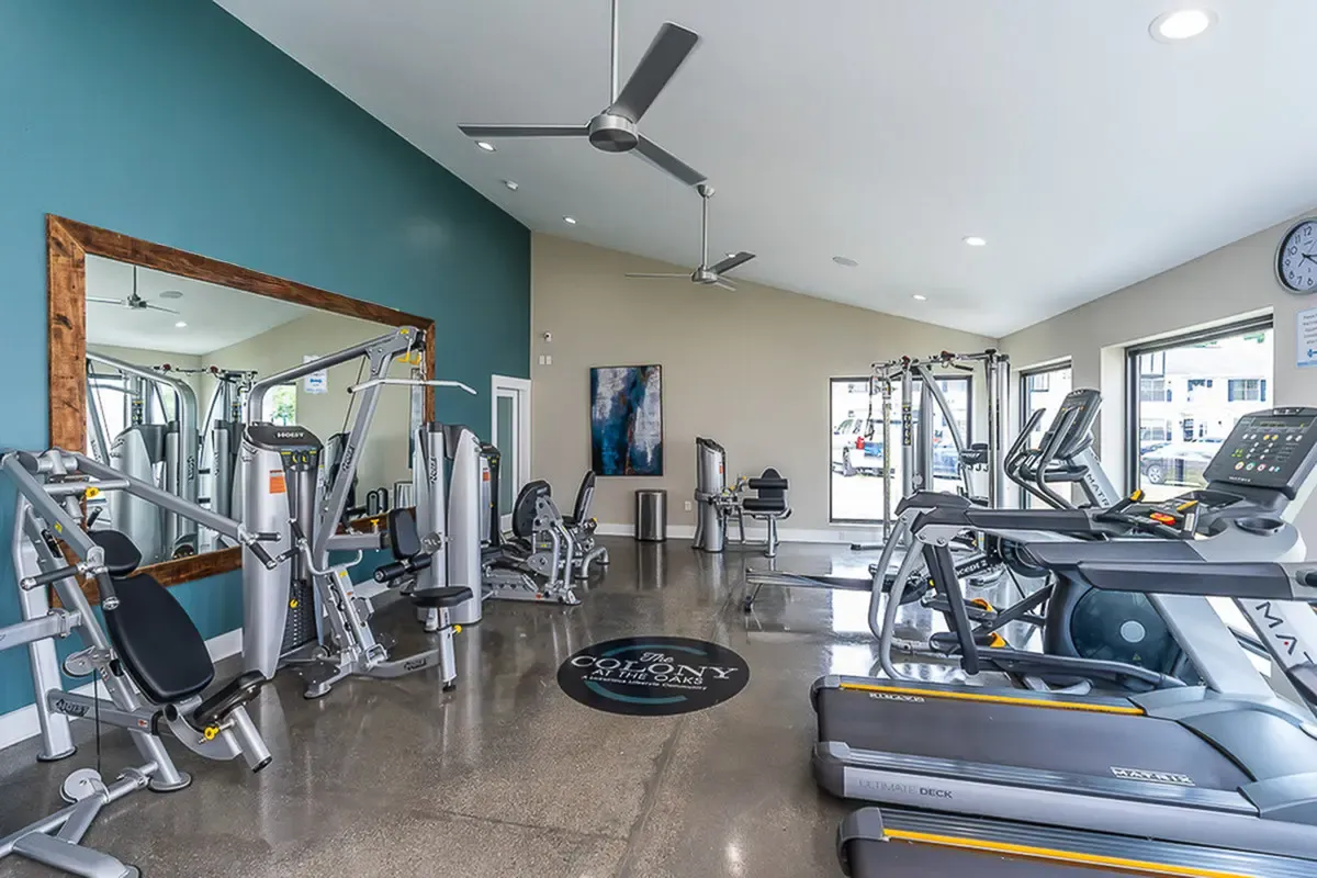 Bright and modern fitness center at The Colony at the Oaks Apartments featuring state-of-the-art equipment and large mirrors, perfect for an energizing workout experience.