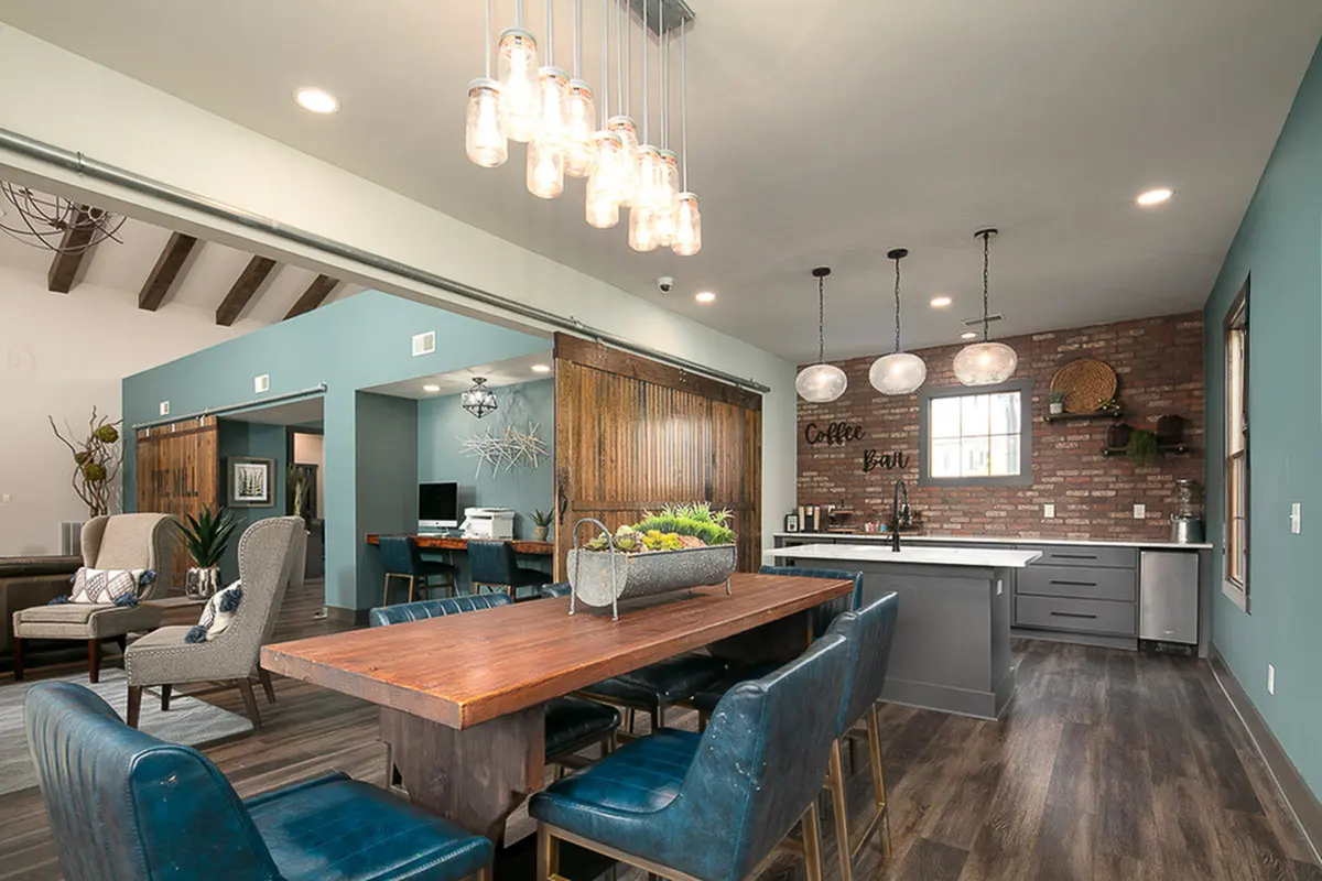 Chic modern interior featuring a rustic dining area with elegant blue seating, warm wooden table, and stylish pendant lighting, adjacent to a trendy kitchen with an exposed brick wall and cozy coffee bar.