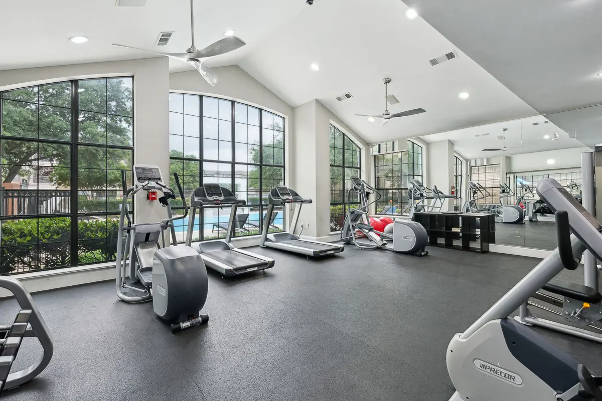Bright and modern fitness center with treadmills and exercise equipment, overlooking a sparkling outdoor pool through large windows.