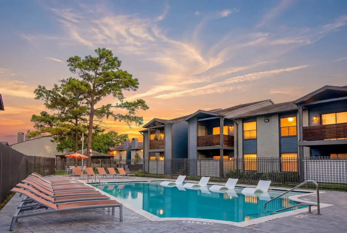 Inviting apartment complex with a luxurious outdoor pool area surrounded by comfortable lounge chairs and vibrant greenery, perfect for relaxation and leisure.