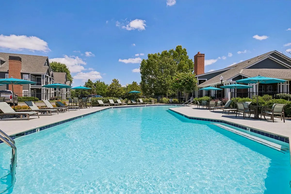 Charming apartment complex with a sparkling pool surrounded by cozy seating and vibrant umbrellas, set against a stunning sunset sky at Cason Apartments in Murfreeboro