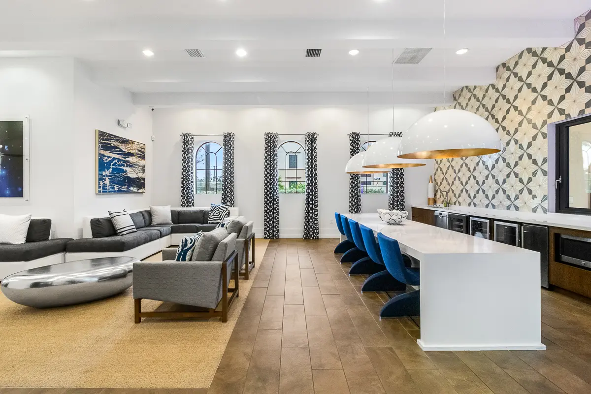 Luxurious clubroom at Cottonwood Lighthouse Point Apartments with modern decor, featuring a sleek white dining table, stylish blue chairs, and elegant lounge seating.