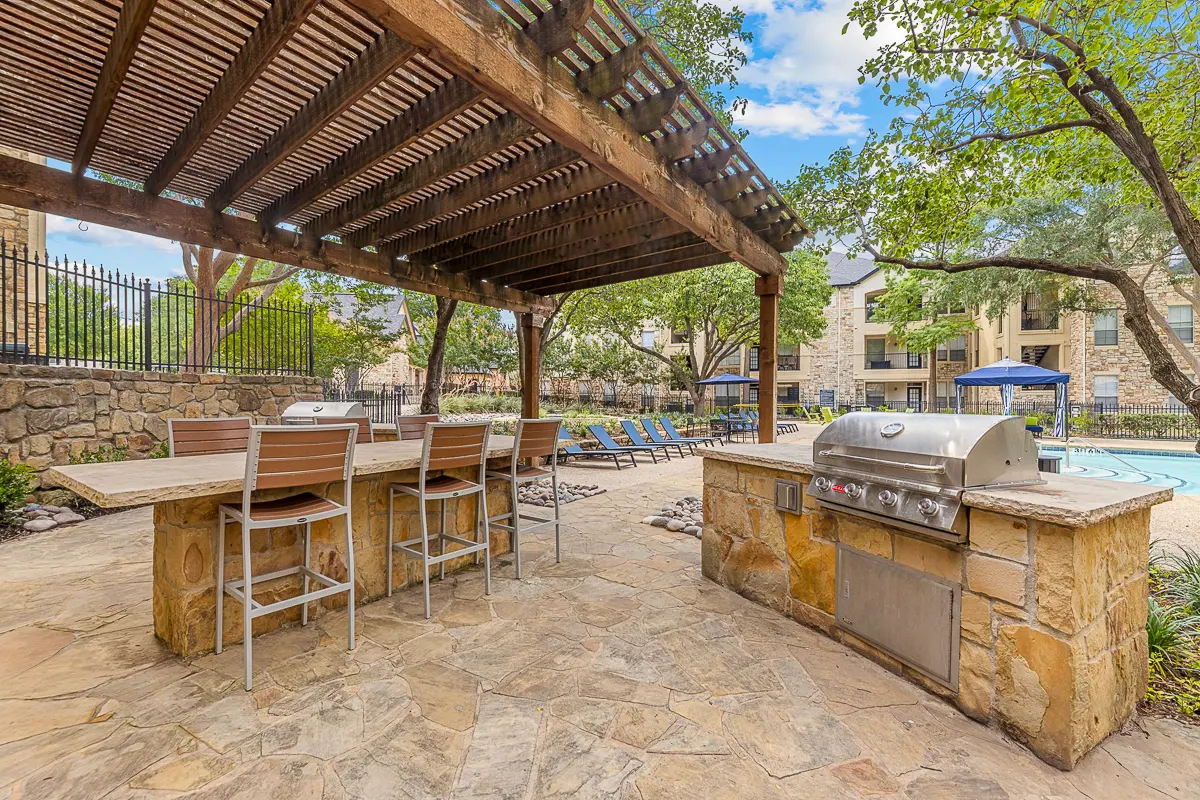 Inviting outdoor patio with grill under a stylish pergola, overlooking a pristine swimming pool and lush, green landscape.