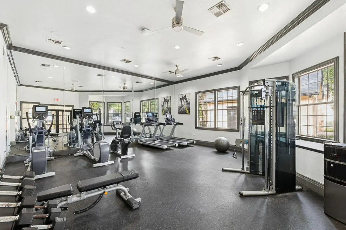 Bright and modern gym with state-of-the-art fitness equipment, including treadmills and a weight rack, in a stylish apartment complex.