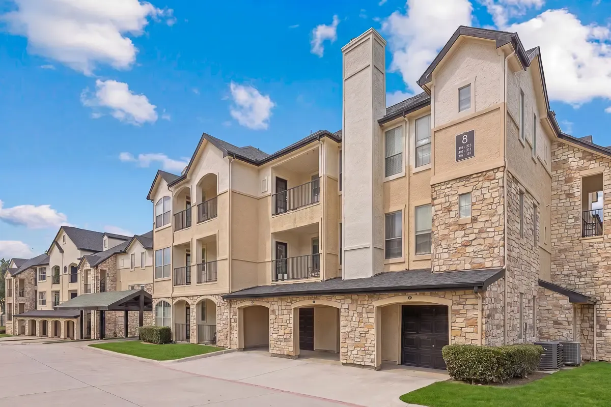 Charming apartment complex with stone facade and manicured lawns under a clear blue sky.