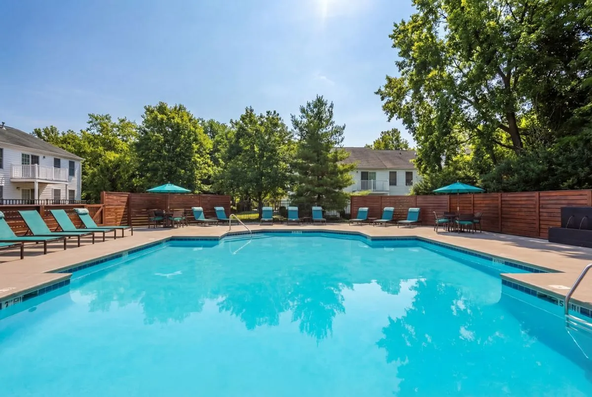 Inviting outdoor pool area with comfortable lounge chairs, shaded tables, and lush green surroundings.