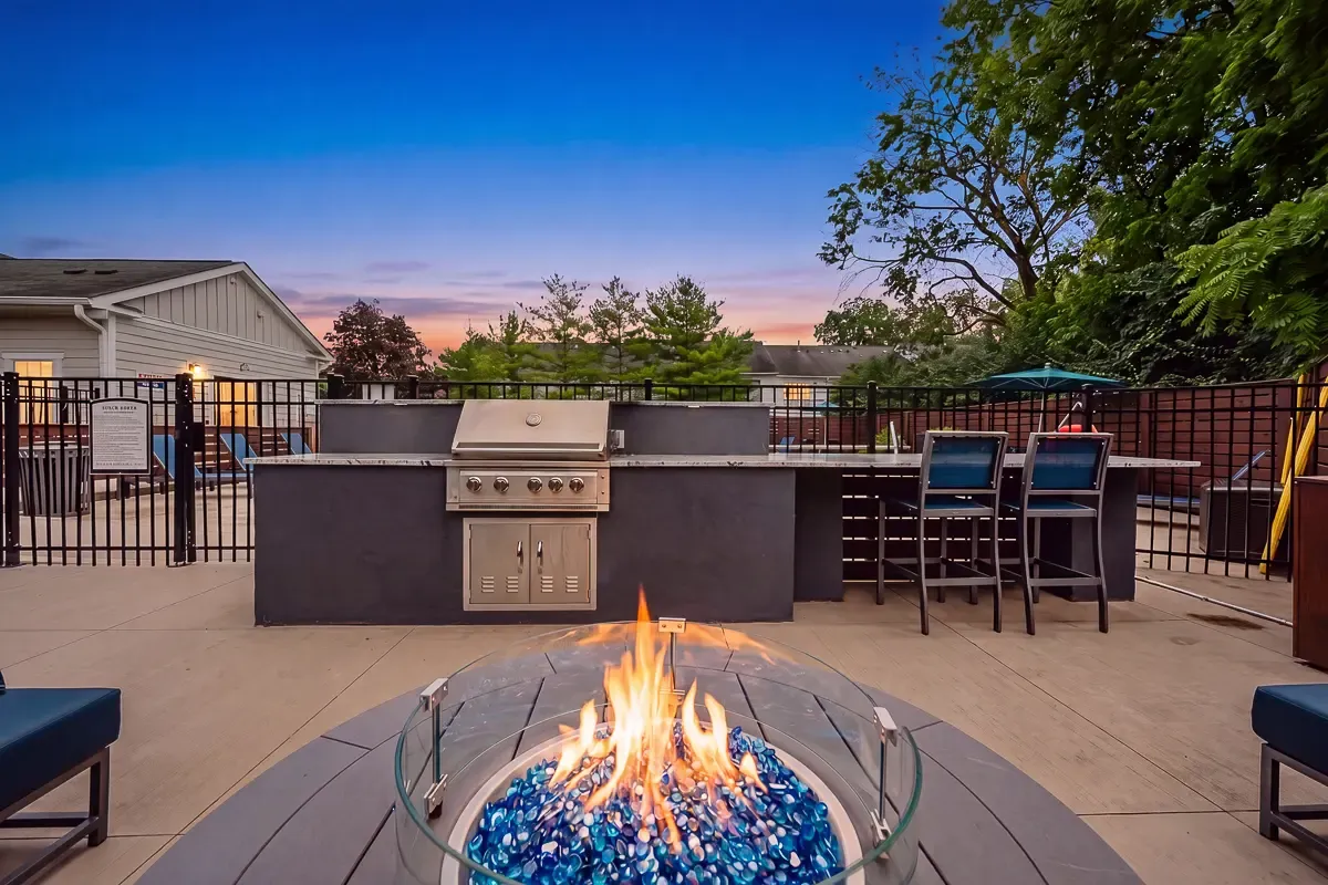 Chic outdoor patio featuring a modern grill station, comfortable seating with turquoise cushions, and a sleek fire pit surrounded by lush greenery.