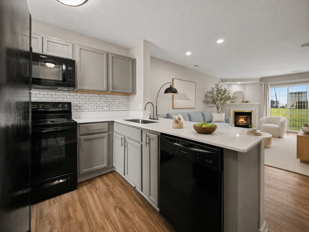 Modern open-concept kitchen and living room with sleek appliances, stylish cabinetry, and a cozy fireplace, overlooking a green outdoor space.