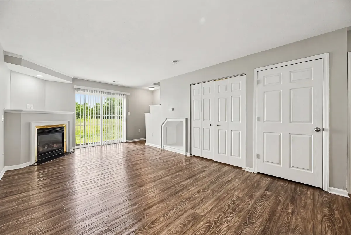 Spacious and modern living room with elegant wooden flooring, featuring a cozy fireplace and large sliding glass doors leading to a lush green view.