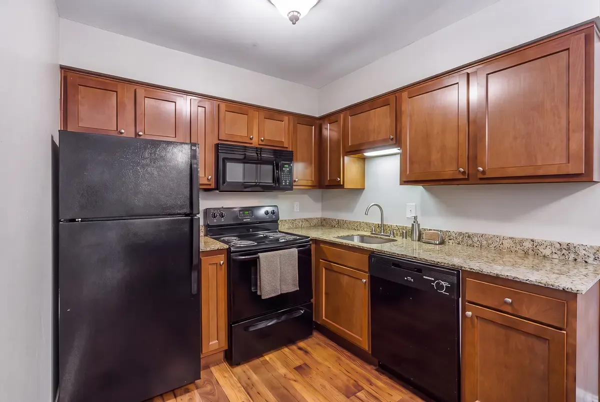 Elegant kitchen at The Creeks on Kirklevington Apartments featuring modern appliances, warm wooden cabinetry, and sleek granite countertops.