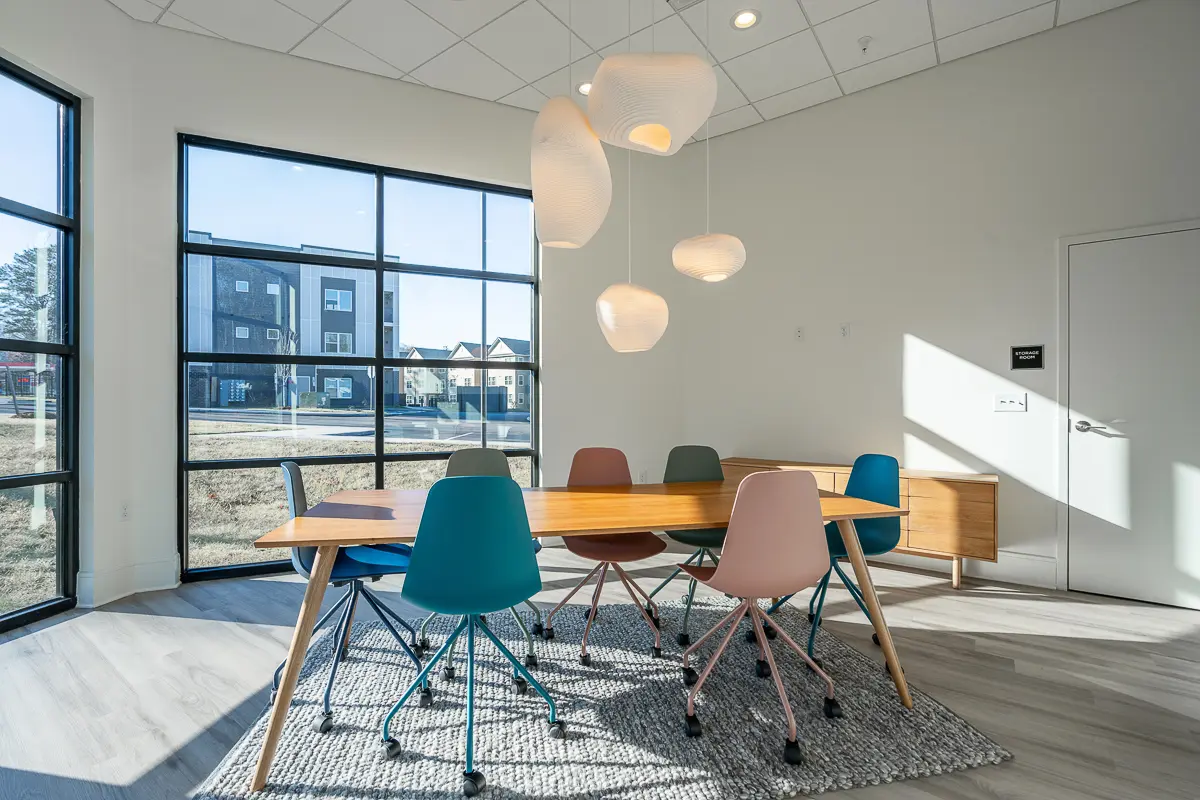 Bright and modern meeting room featuring colorful chairs, a large window with natural light, and elegant pendant lighting.