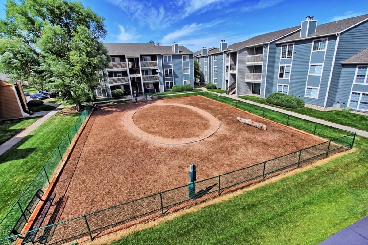 Charming apartment complex with well-maintained grounds, featuring a spacious fenced area surrounded by lush greenery and modern buildings.