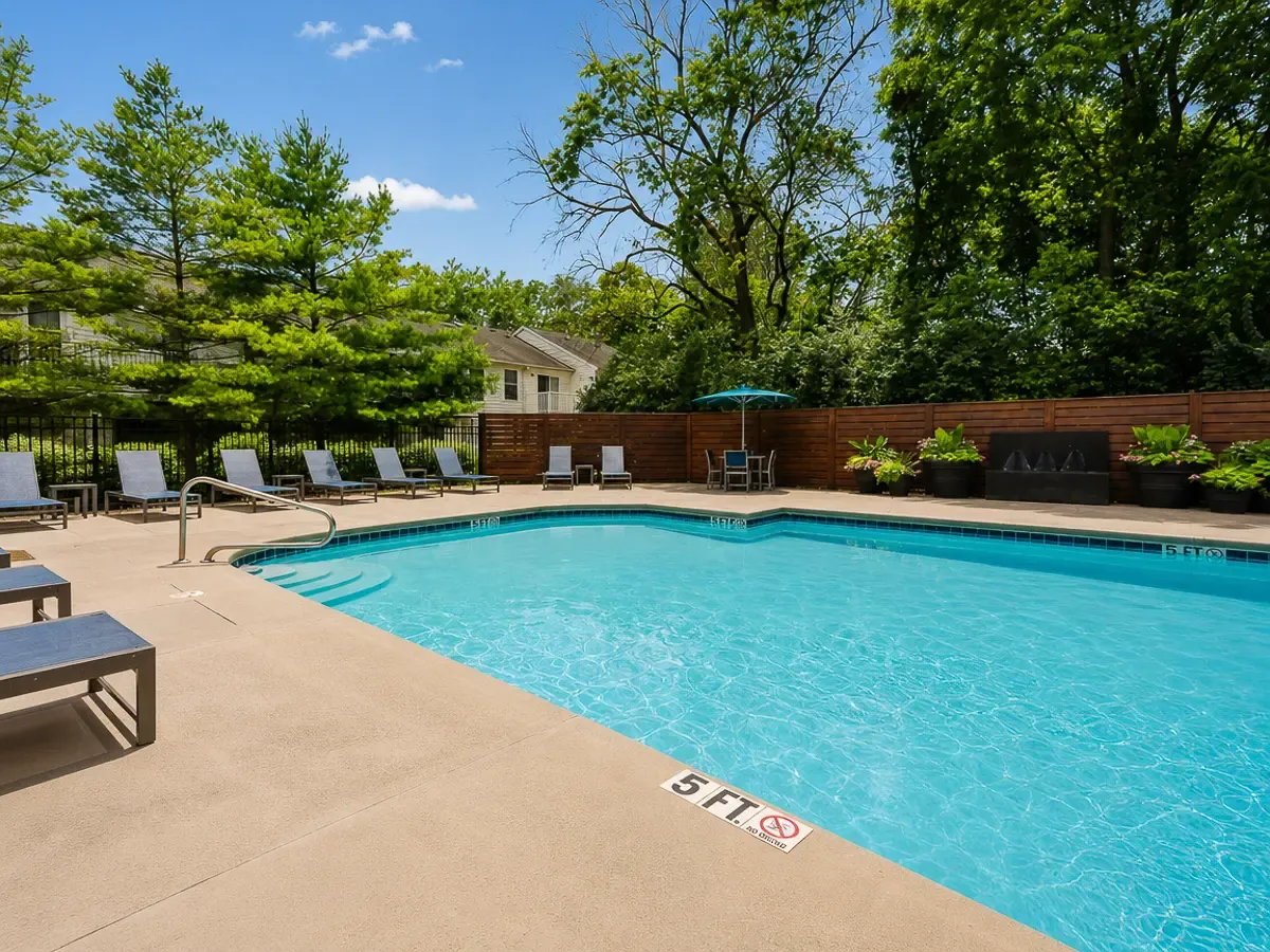 Inviting outdoor pool area with comfortable lounge chairs, shaded tables, and lush green surroundings.