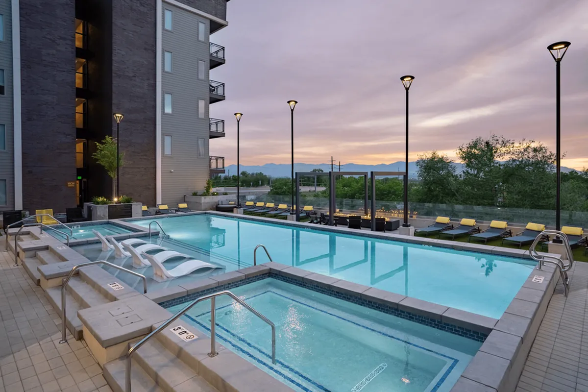 Elegant outdoor pool area with modern lounge chairs, set against a stunning sunset view and mountain backdrop, perfect for relaxation and entertainment.