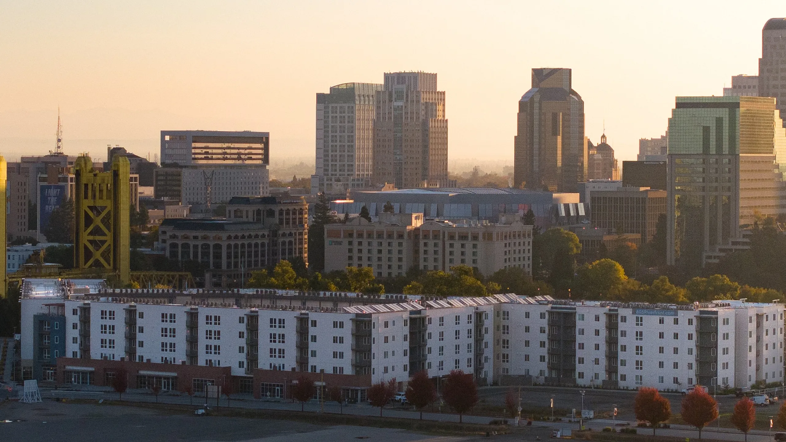 Panoramic view of a vibrant city skyline at sunset, featuring modern high-rise buildings and a prominent yellow bridge at 805 Riverfront Apartments