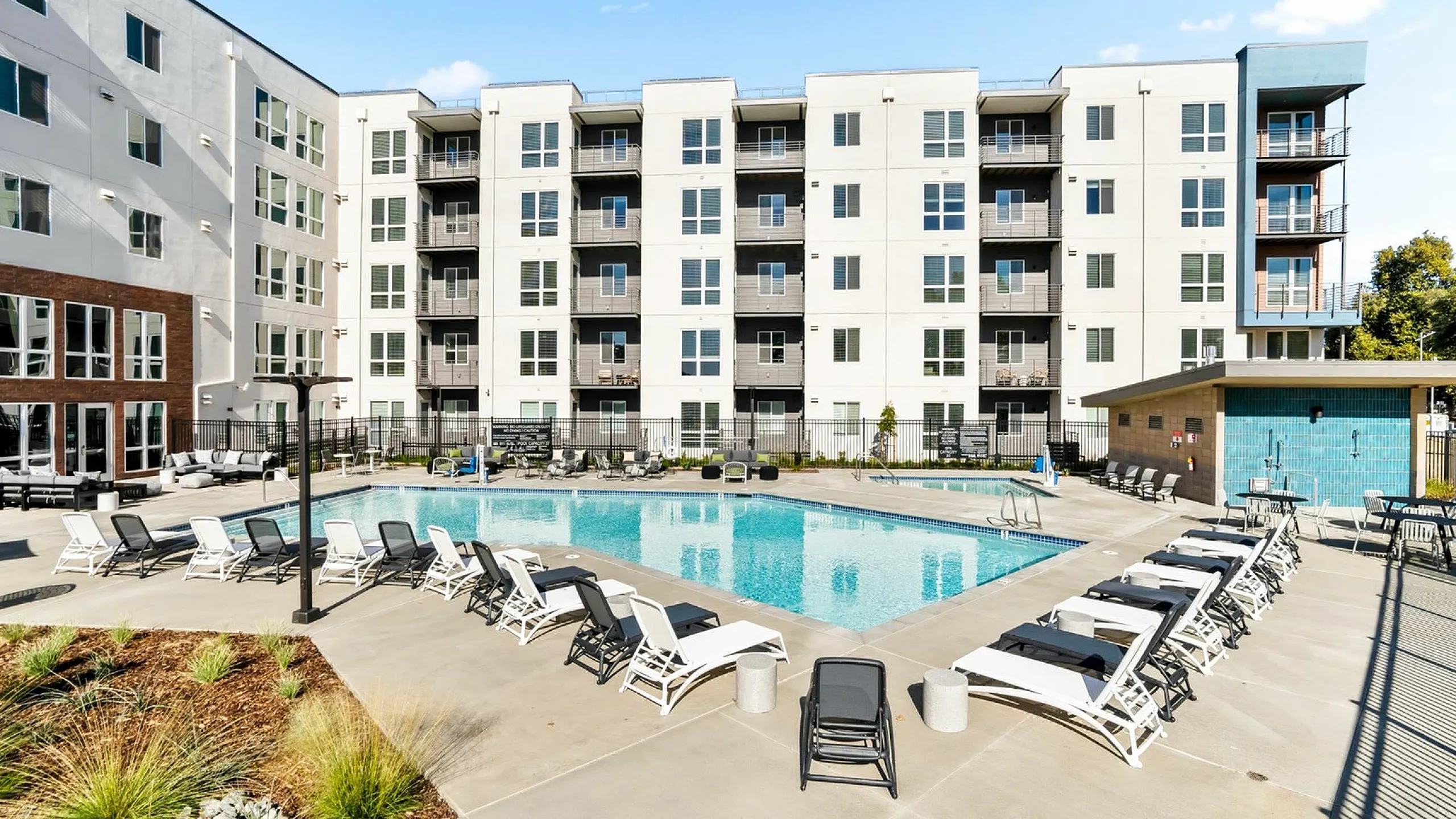 Modern apartment complex with spacious balconies overlooking a luxurious outdoor pool area, surrounded by stylish lounge chairs for ultimate relaxation.