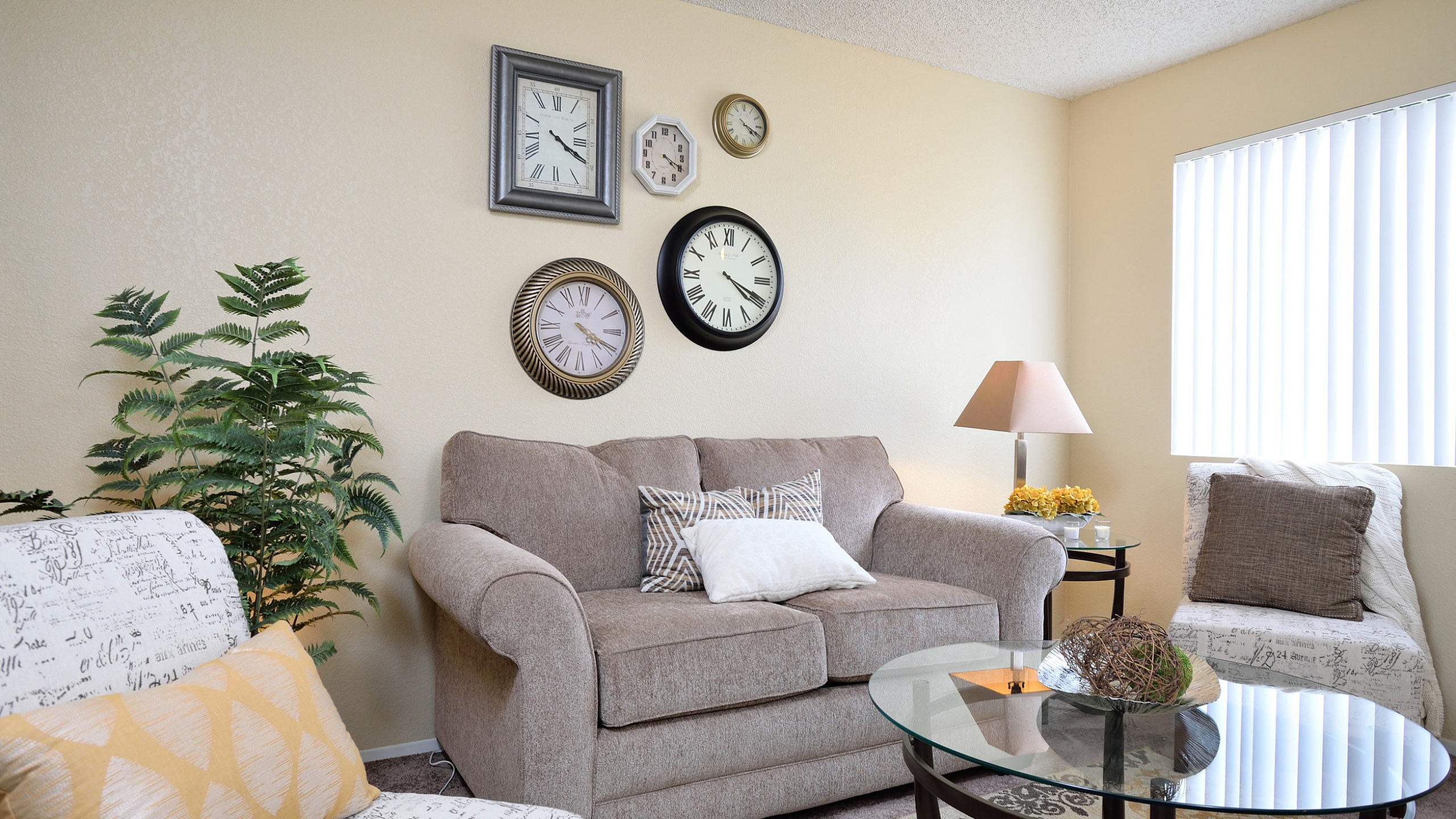 Cozy living room at Camelot Apartments with stylish decor, featuring a plush sofa, chic wall clocks, elegant glass coffee table, and inviting ambient lighting.