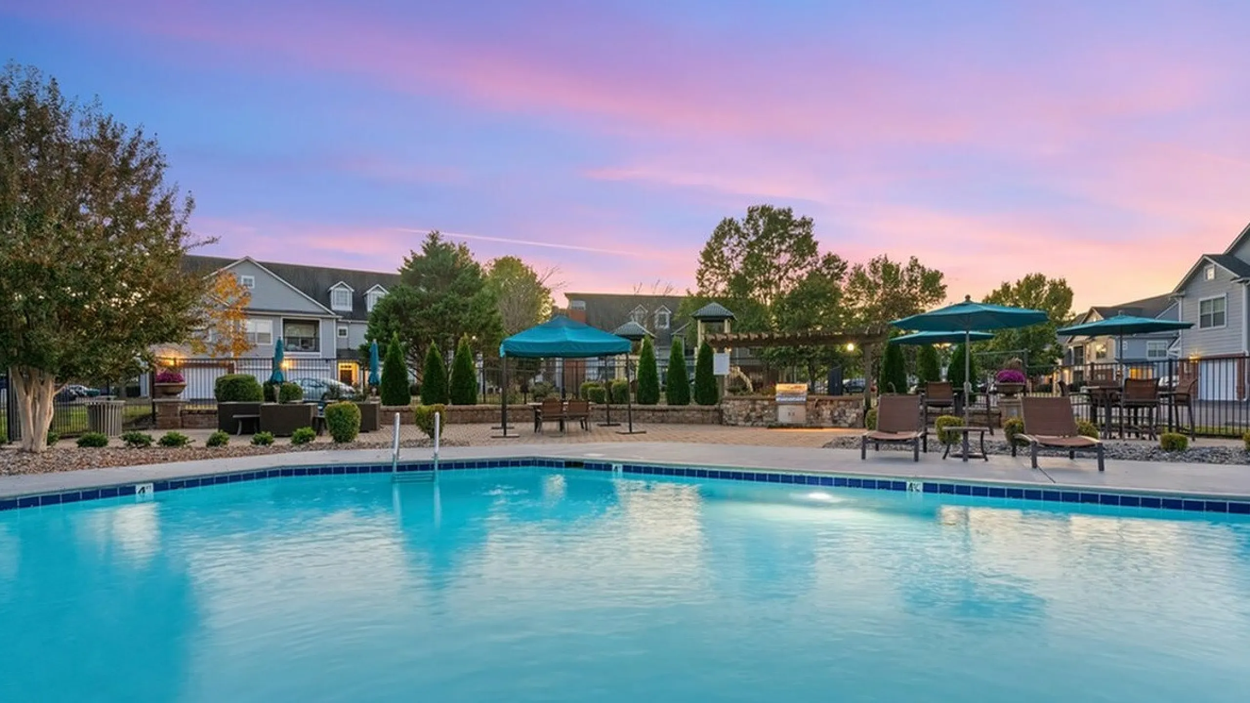 Luxurious apartment complex, Cason Estates Apartments, with serene poolside view at sunset, featuring inviting loungers and stylish blue umbrellas.