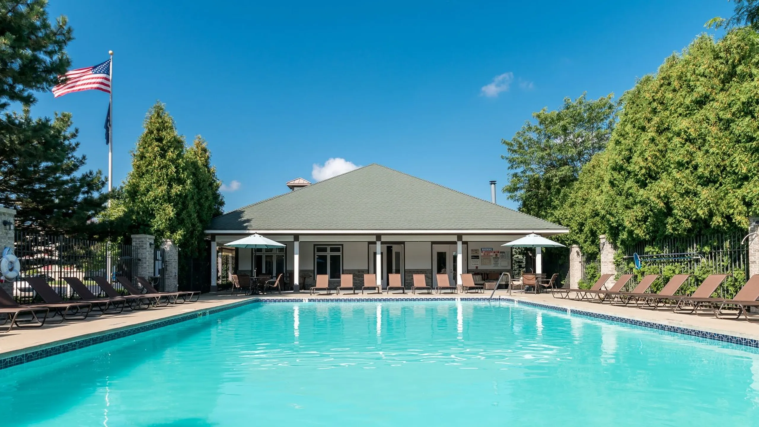 Inviting outdoor pool area at Clearview Apartments in Holland, MI with comfortable lounge chairs and green surroundings under a clear blue sky.