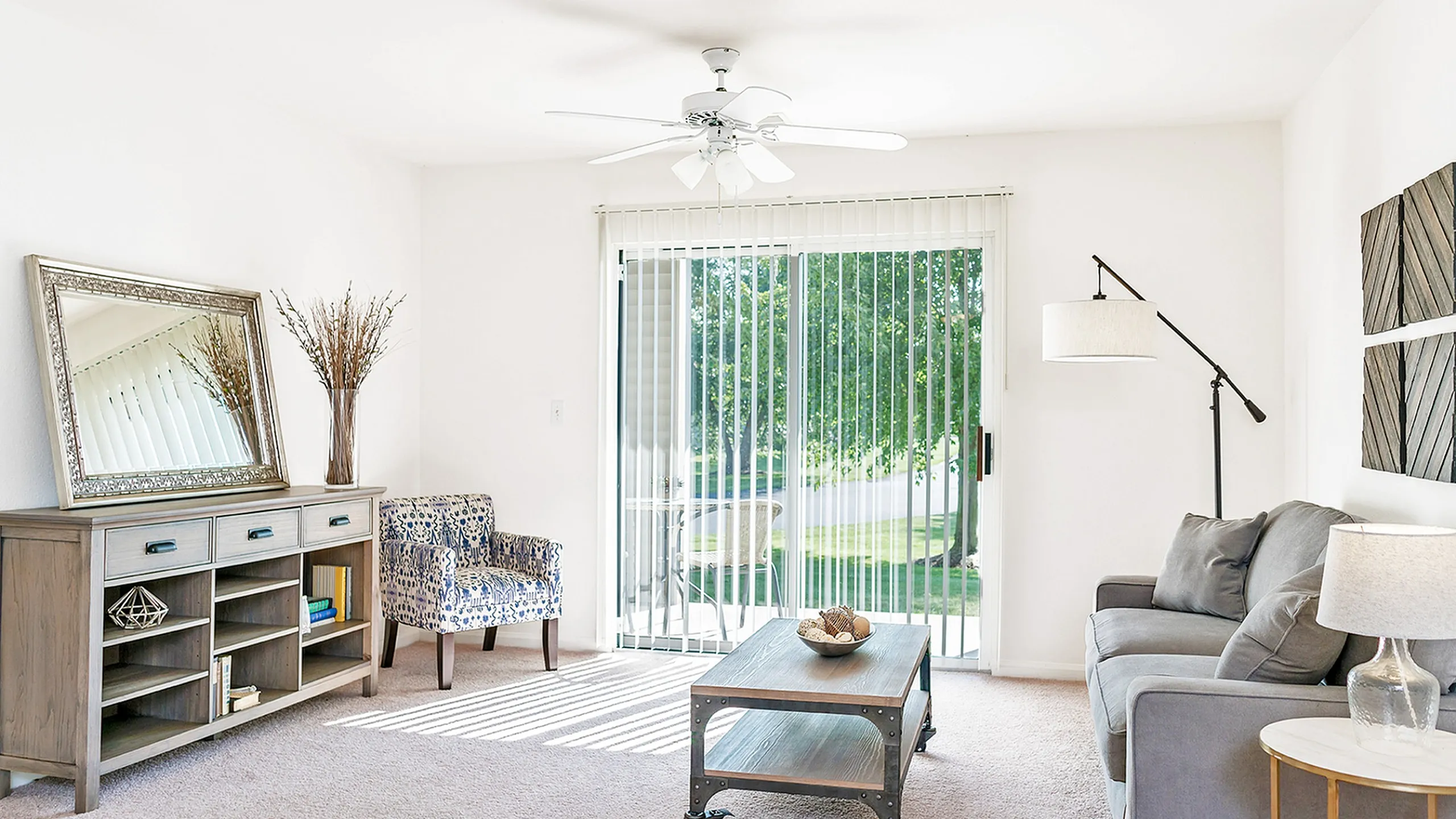 Bright, inviting living room at Clearview Apartments with plush gray sofa, chic decor, and serene outdoor view through large glass doors.