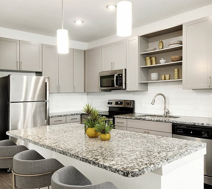 Modern kitchen at Cottonwood Clermont Apartments with sleek stainless steel appliances, granite countertops, and elegant light fixtures, perfect for gourmet cooking.