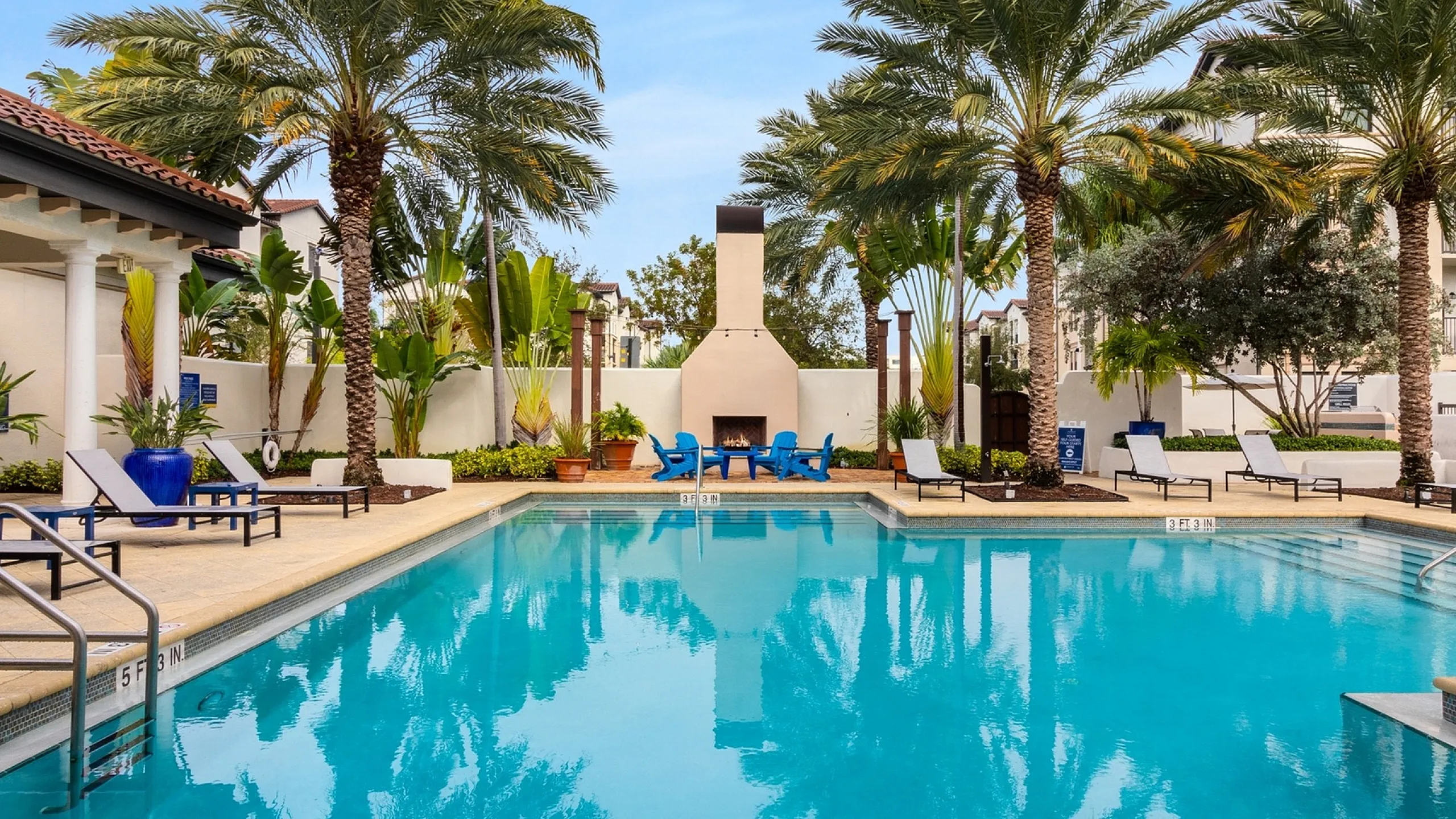 Luxurious outdoor pool area with palm trees, lounge chairs, and a cozy outdoor fireplace, perfect for relaxation and leisure at Cottonwood Lighthouse Point in Pompano Beach