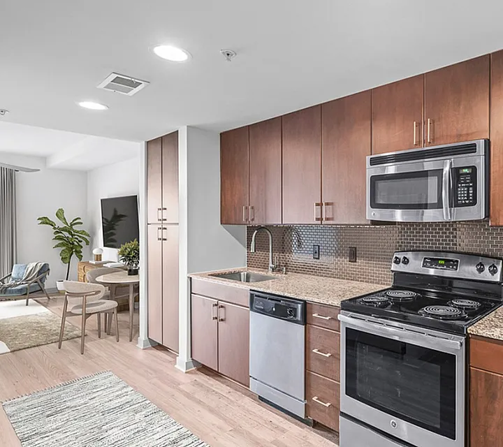 Modern kitchen at Cottonwood Westside in Midtown Atlanta with sleek stainless steel appliances, rich wood cabinets, and an elegant open-concept dining area featuring a stylish plant accent.