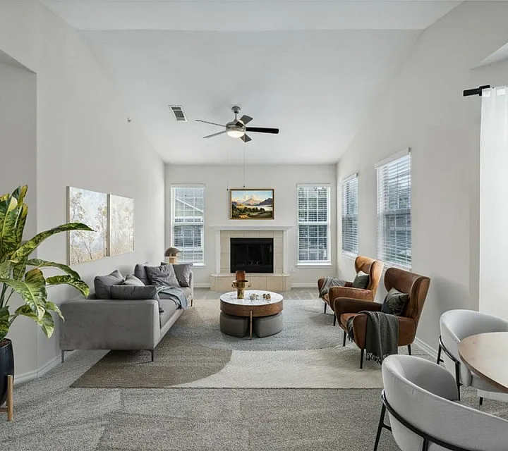 Bright, elegant living room with modern gray sofa, cozy armchairs, and lush green plant near a classic fireplace, perfect for relaxation at Cottonwood Ridgeview Apartments for Rent in Plano Texas