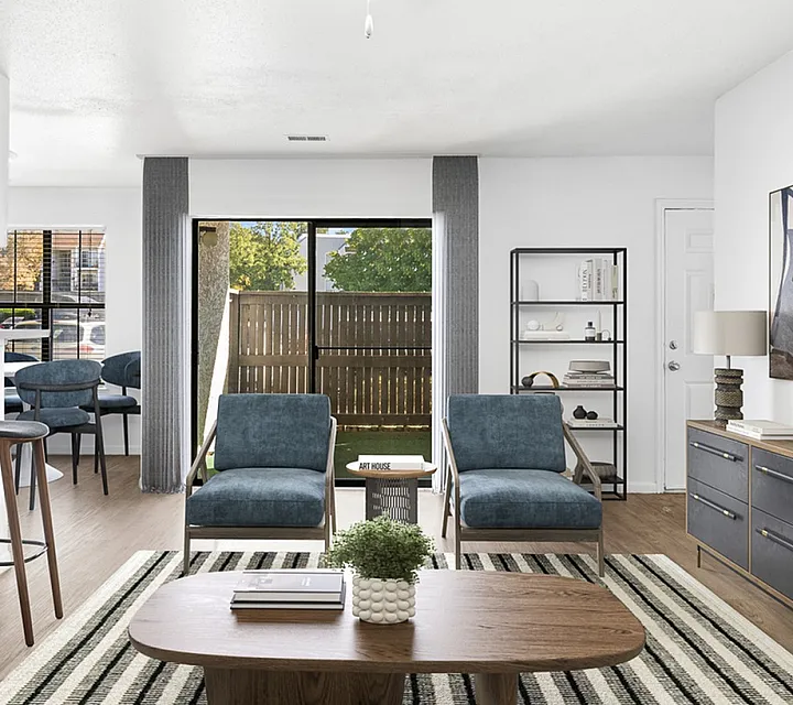 Modern living space at Cottonwood Apartments with chic blue chairs, natural lighting, stylish art, and a cozy open concept feel.