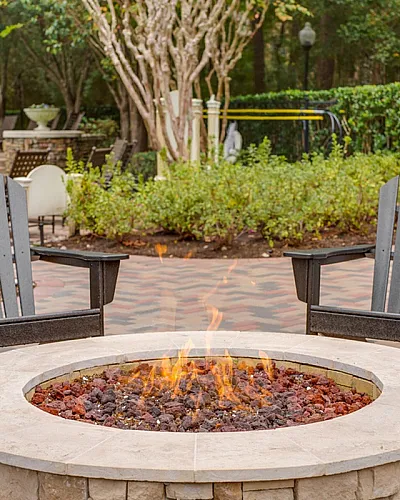 Inviting outdoor patio featuring a cozy fire pit surrounded by comfortable Adirondack chairs, perfect for relaxing in a serene garden setting at Raveneaux Apartments in Houston