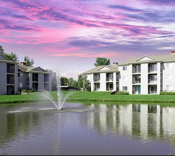 Charming apartments in Holland Michigan with serene pond, stunning sunset sky, and lush green landscaping at Clearview Apartments