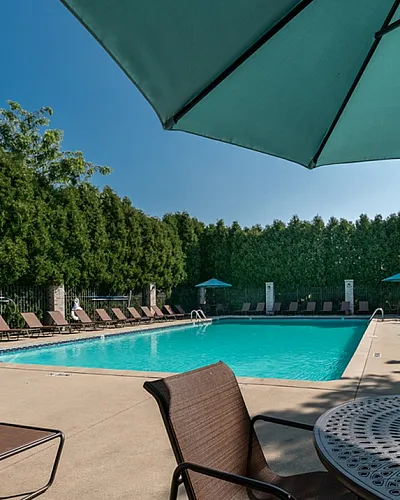Inviting swimming pool area with cozy lounge chairs and lush greenery under a clear blue sky at Clearview Apartments in Holland Michigan