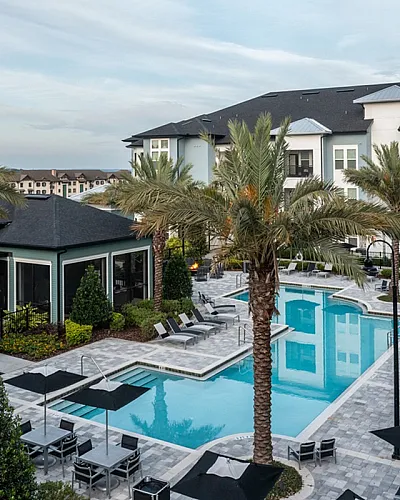 Luxurious apartment complex showcasing a stunning pool area with elegant cabanas and lush palm trees, offering a resort-style living experience at Cottonwood Clermont Apartments