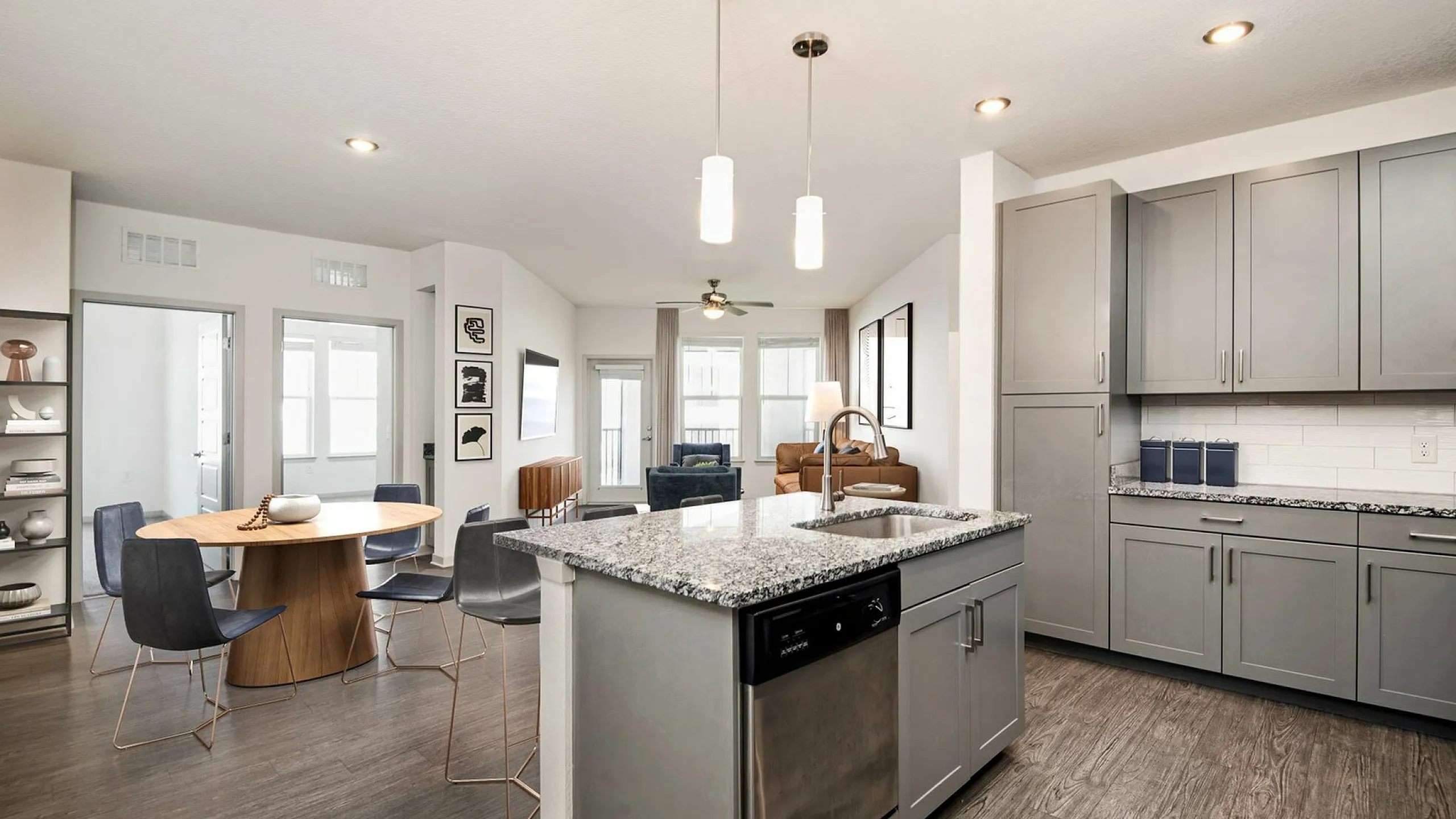 Bright and modern open-concept kitchen and dining area with sleek gray cabinets, granite countertops, and stylish pendant lighting, perfect for entertaining at Cottonwood Clermont Apartments