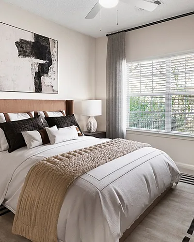 Elegant bedroom with modern decor, featuring a plush bed, contemporary art, and a large window with natural light.